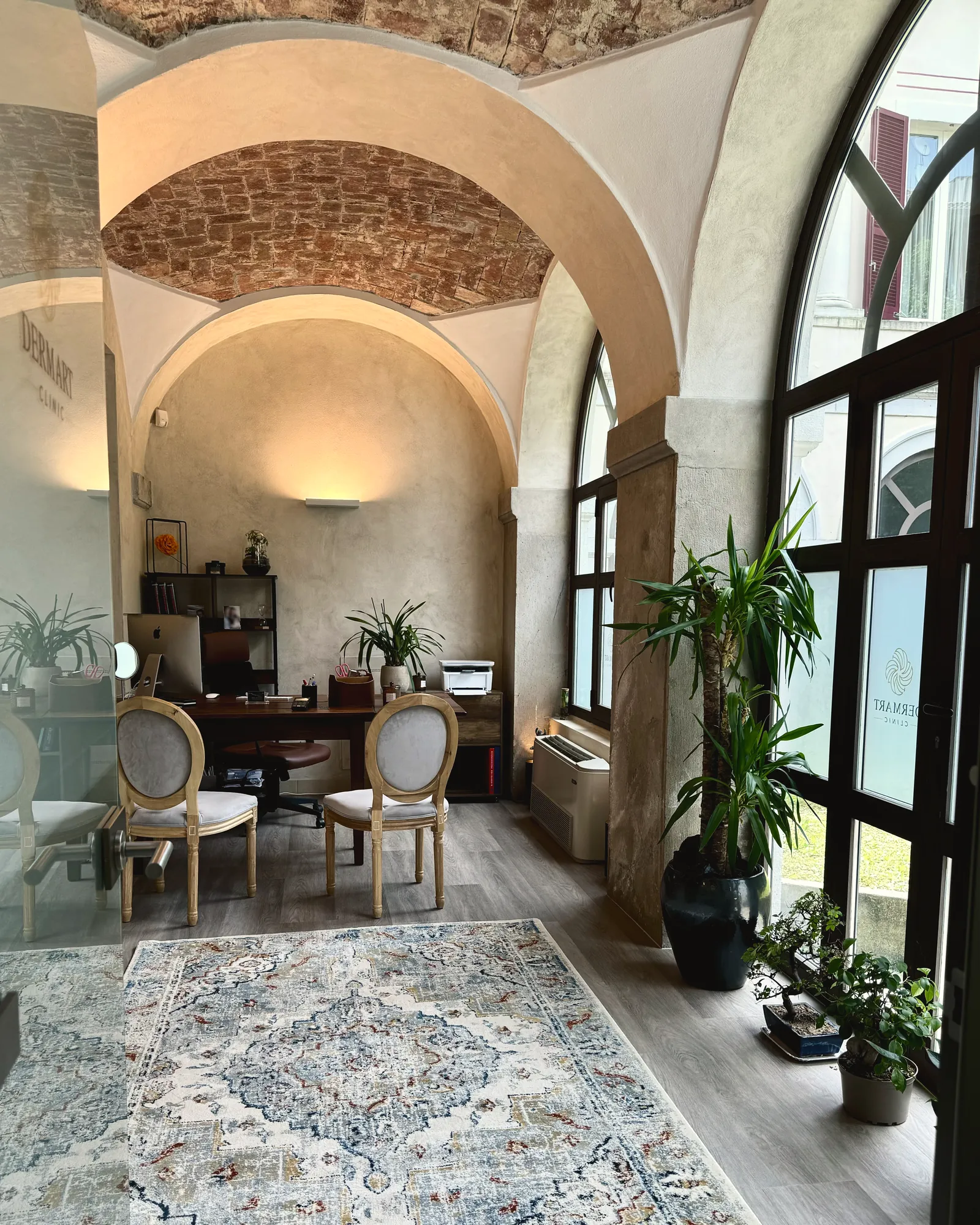 Lo studio di Derm Art Clinic in via Donizetti 4 a Varese: volte a crociera in mattoni, archi, una grande finestra ad arco sul cortile, la scrivania e due sedie a medaglione.