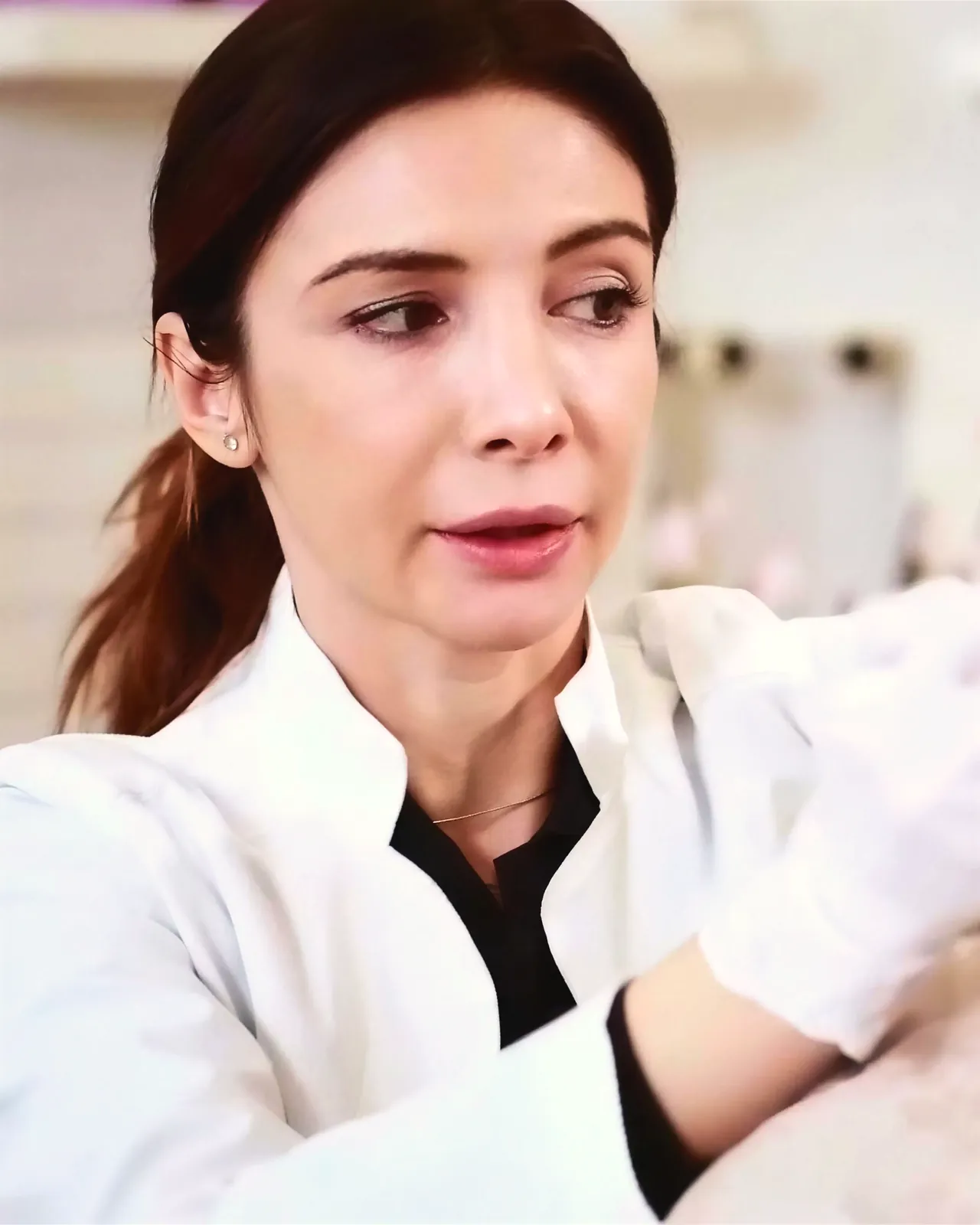 La Dott.ssa Laura Balint in camice bianco guarda le proprie mani guantate mentre prepara un trattamento.
